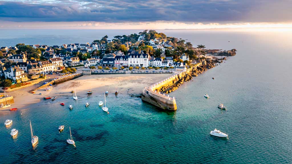 Photo aérienne du port de Loquirec dans le Finistère, montrant les bateaux amarrés, la digue et les eaux claires de la côte bretonne.