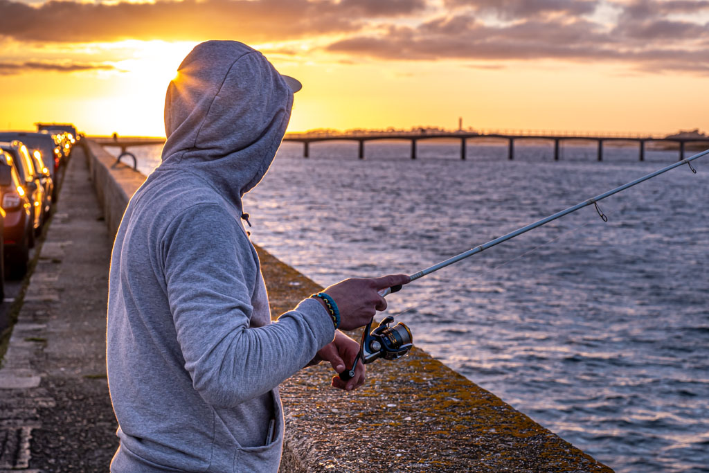 Jeune homme blond pêchant devant l’estacade de Roscoff au coucher du soleil