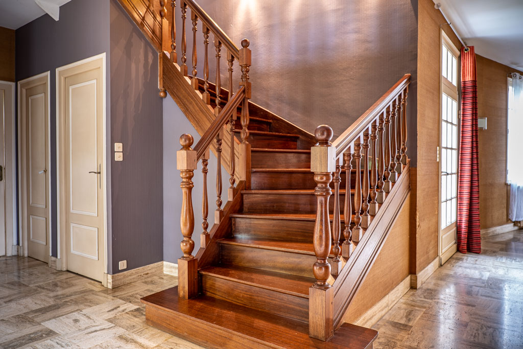Photo immobilière : détail architectural d’un escalier en bois avec marches et rambarde sculptée